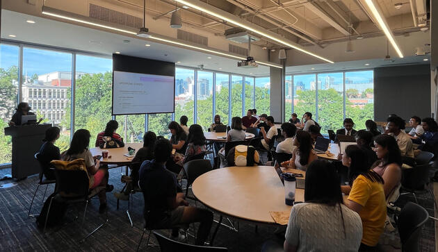 A picture of Shirley speaking and presenting slides in a room full of students